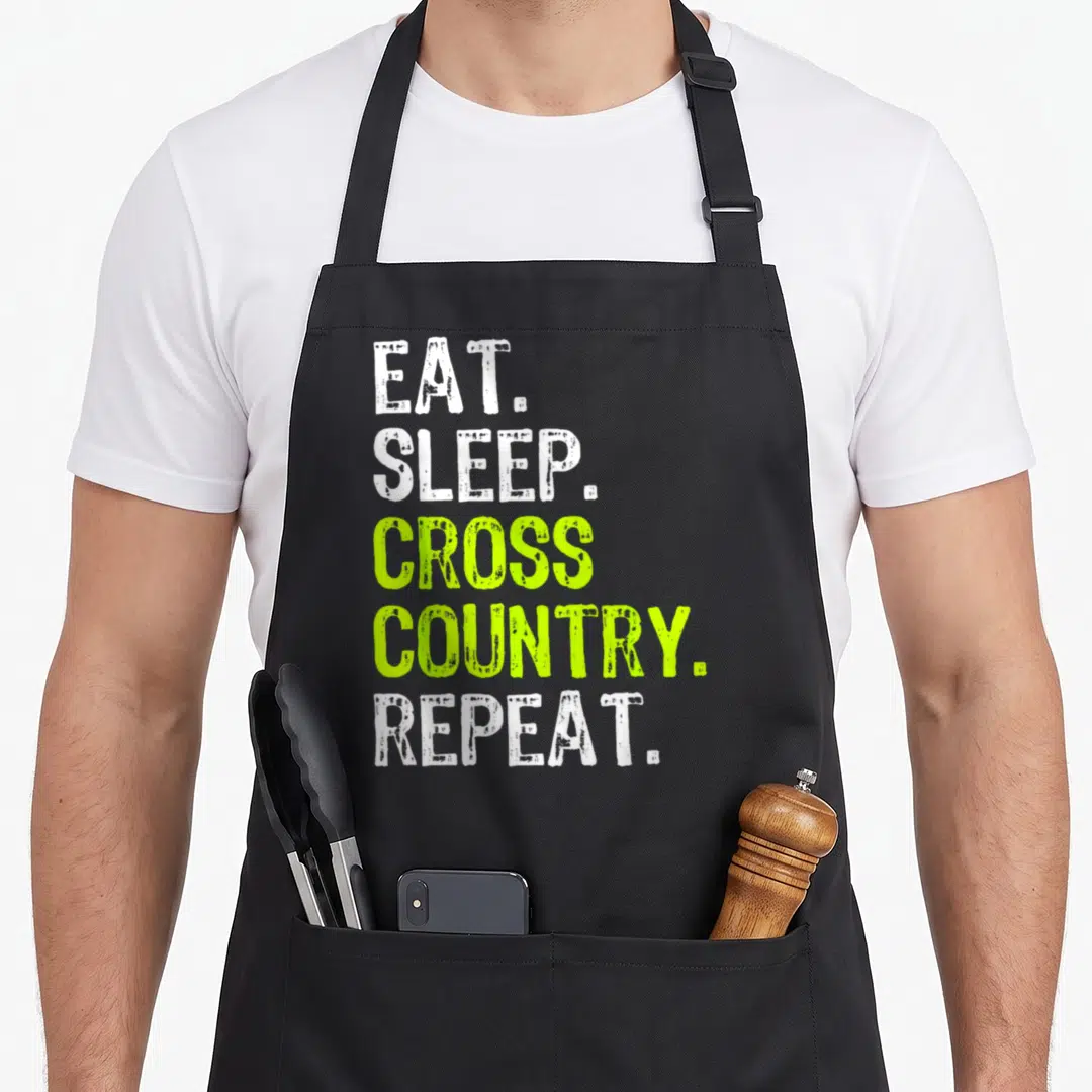 Eat country apron - Stacked EAT SLEEP CROSS COUNTRY REPEAT text in white and lime green on black — shown on a black cotton canvas apron against a white background