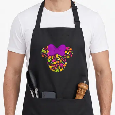 Icon halloween apron - Purple bow over mouse head shape filled with orange pumpkins, candy, and spider webs — shown on a black cotton canvas apron against a white background