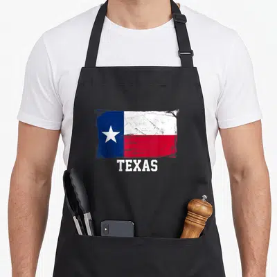 Distressed texas apron - Distressed blue white and red Texas flag print with white block lettering below — shown on a black cotton canvas apron against a white background