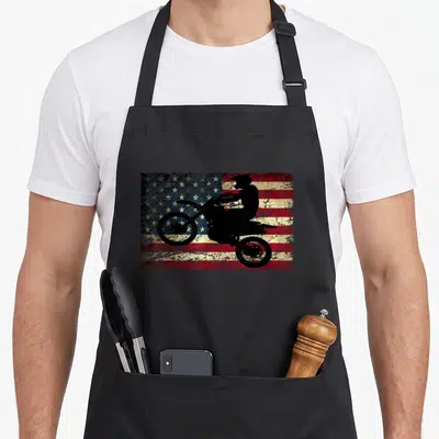 Bike american flag apron - Black motocross rider silhouette on distressed red white and blue American flag background — shown on a black cotton canvas apron against a white background