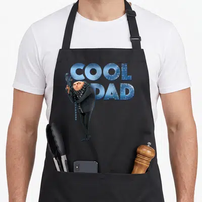 Gru despicable me apron - Gru holding freeze ray next to blue COOL DAD text on black background — shown on a black cotton canvas apron against a white background