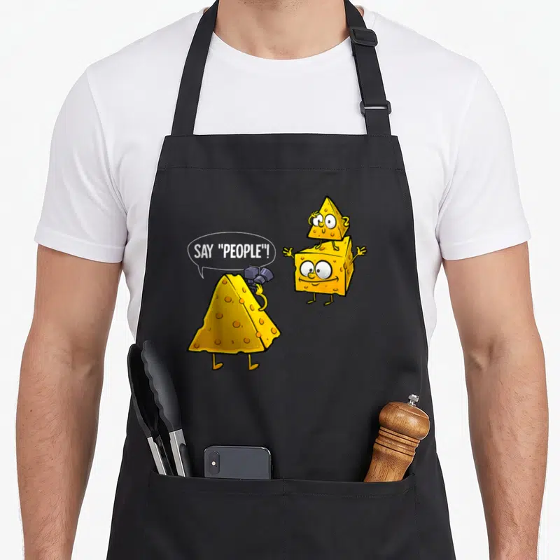 Cheese photographer apron - Cartoon yellow cheese wedge holding camera says Say People next to two stacked cheese blocks — shown on a black cotton canvas apron against a white background