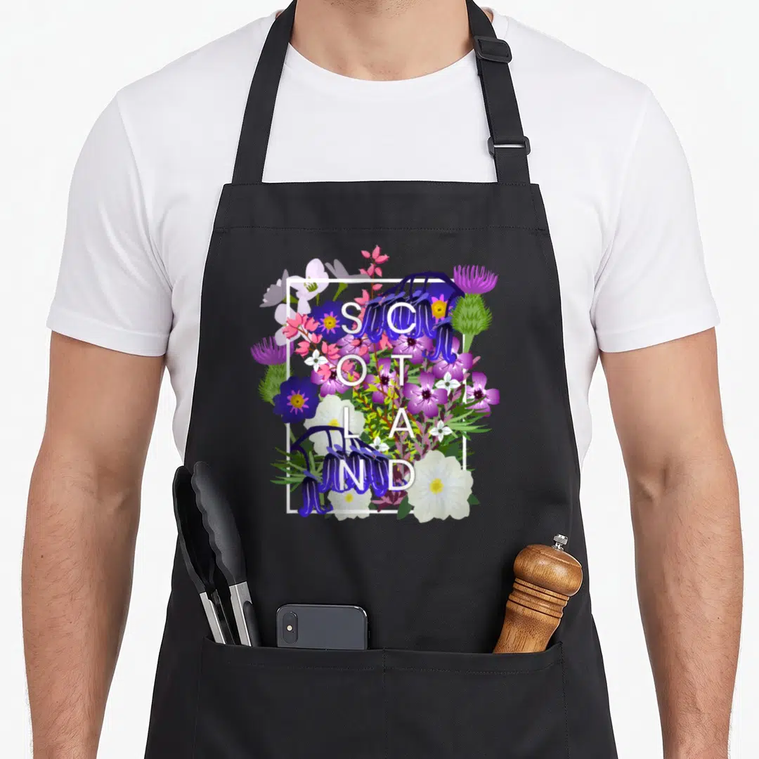 Flower pride apron - SCOTLAND text over purple blue pink white flowers in white square frame — shown on a black cotton canvas apron against a white background