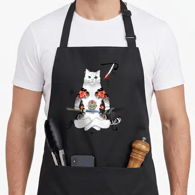 Yakuza cat apron - Tattooed white cat holding katana with hannya mask and Japanese characters — shown on a black cotton canvas apron against a white background