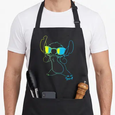 Stitch outline of an apron - Cartoon alien figure outline in blue and yellow gradients wearing sunglasses with STITCH — shown on a black cotton canvas apron against a white background
