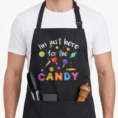 Costume lollipop halloween apron - I'm just here for the CANDY text with colorful swirls, hearts, and bubbles on black — shown on a black cotton canvas apron against a white background