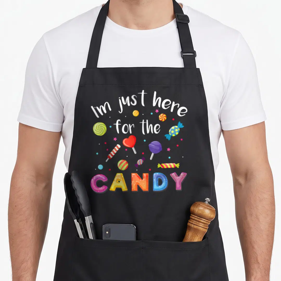 Costume lollipop halloween apron - I'm just here for the CANDY text with colorful swirls, hearts, and bubbles on black — shown on a black cotton canvas apron against a white background