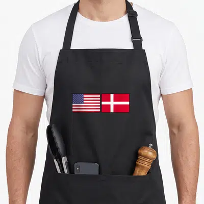Hygge american flag apron - Two rectangular flags side by side, US and Denmark, red white blue minimalist — shown on a black cotton canvas apron against a white background