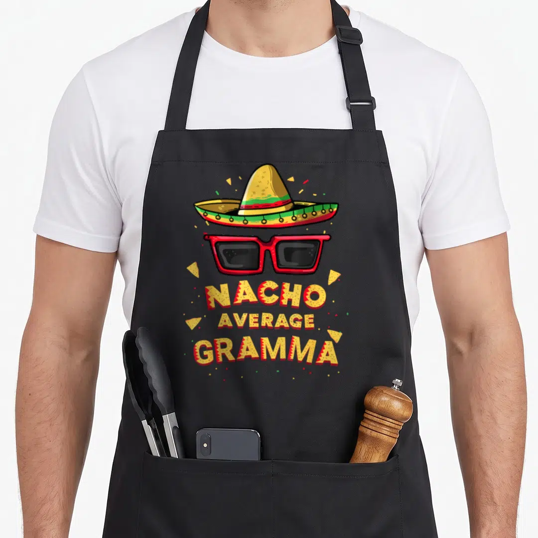 Gramma mexican apron - Sombrero sunglasses and Nacho Average Gramma text with tortilla chips in yellow red green — shown on a black cotton canvas apron against a white background