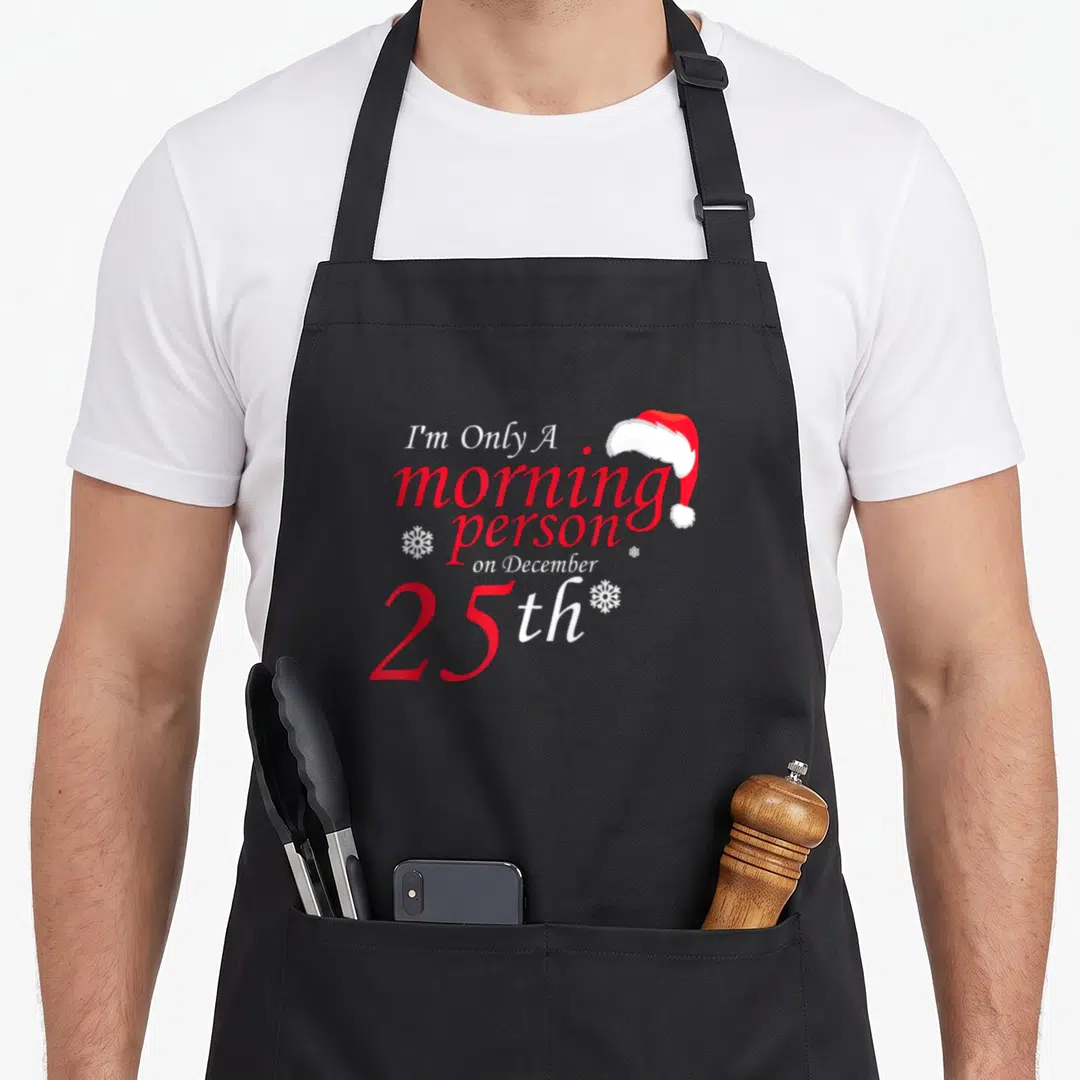 25th women's christmas apron - Red and white text I'm Only A morning person on December 25th with Santa hat — shown on a black cotton canvas apron against a white background