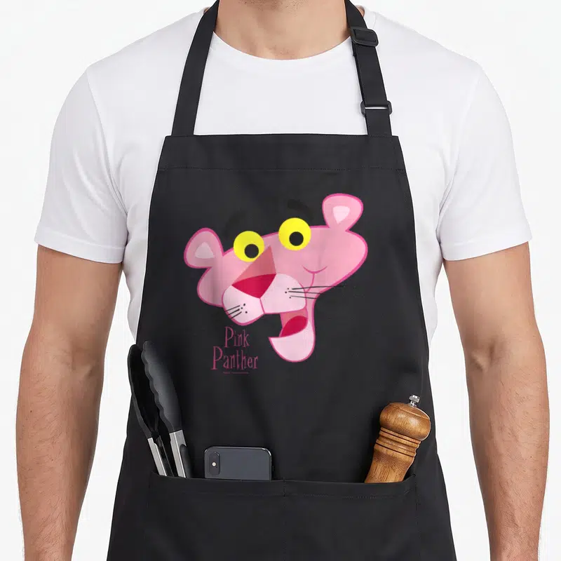 Funny portrait face apron - Pink Panther cartoon head with yellow eyes and stacked pink text below chin — shown on a black cotton canvas apron against a white background