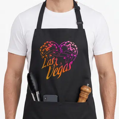 Pot theme aprons - Heart shape formed by slot machines and dollar sign with Las A, Vegas text in orange pink magenta — shown on a black cotton canvas apron against a white background