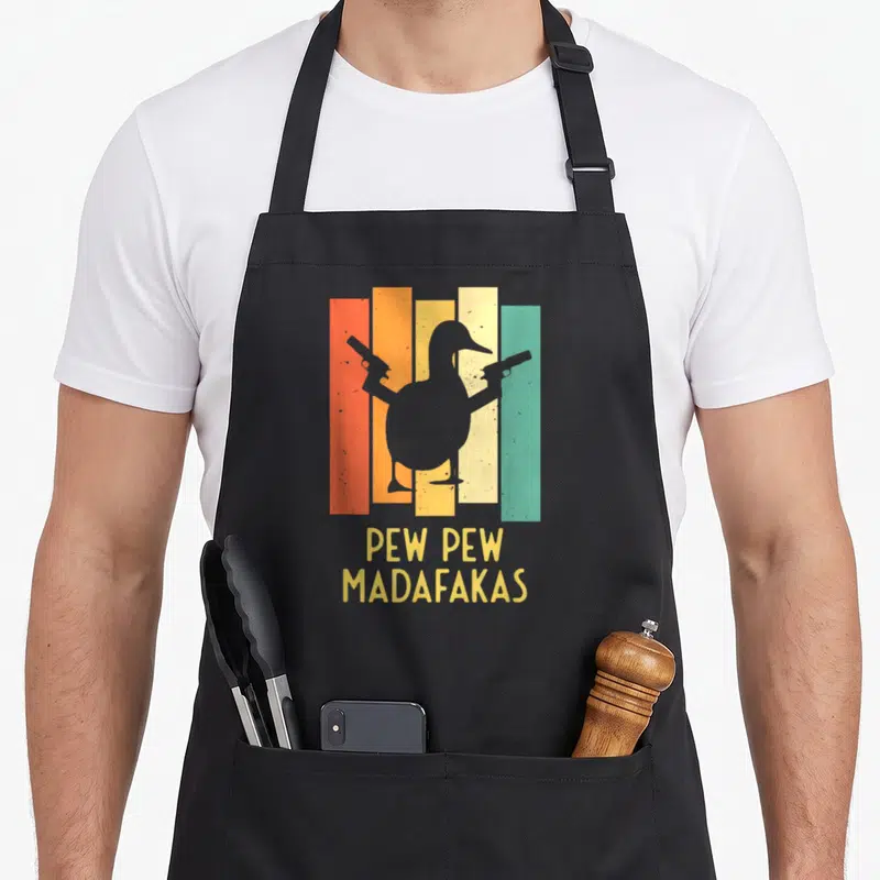 Pistol cotton duck aprons - Grey duck silhouette holding two guns over orange, yellow, teal, and grey stripes with text — shown on a black cotton canvas apron against a white background