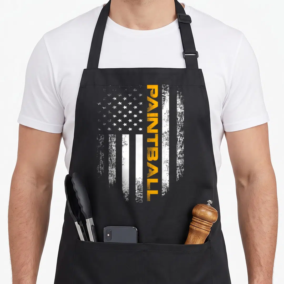 Paintball sport american flag apron - Vertical orange PAINTBALL text over distressed white stars and stripes flag — shown on a black cotton canvas apron against a white background