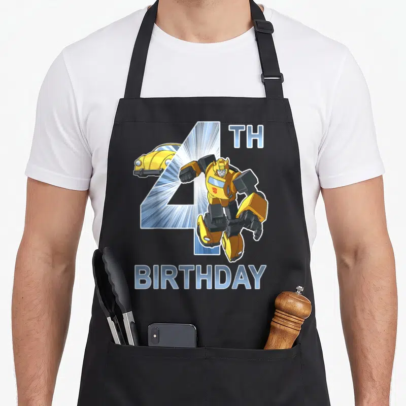 Bumblebee birthday apron - Leaping robot in front of blue number 4 with yellow car and 4TH BIRTHDAY text — shown on a black cotton canvas apron against a white background