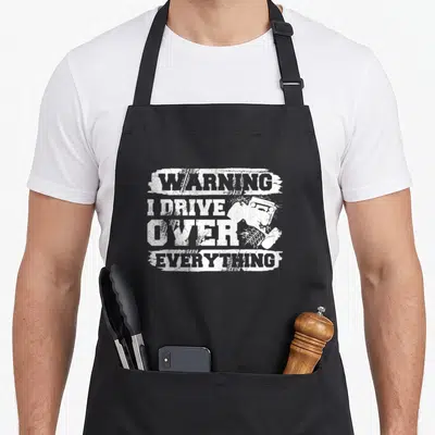 Crawling crawler apron - White stacked text WARNING I DRIVE OVER EVERYTHING with off-road vehicle and tire tracks — shown on a black cotton canvas apron against a white background