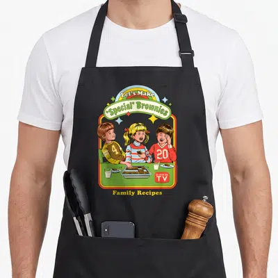 Browny special aprons - Three children eating brownies at green table under rainbow and Let's Make Special Brownies text — shown on a black cotton canvas apron against a white background