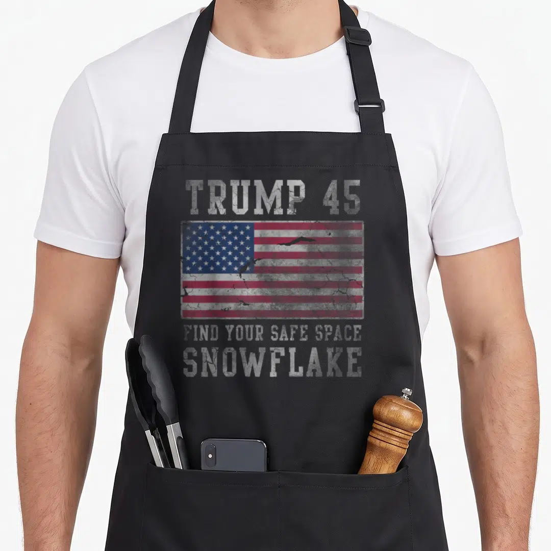 Trump safe apron - Distressed USA flag with TRUMP 45 FIND YOUR SAFE SPACE SNOWFLAKE text in red white blue — shown on a black cotton canvas apron against a white background