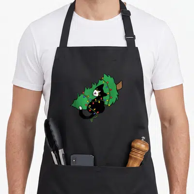 Meowy tuxedo apron - Black cat tangled in red yellow blue lights pushing over green Christmas tree cartoon — shown on a black cotton canvas apron against a white background