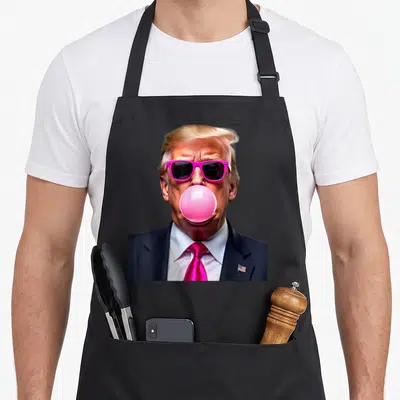 Trump funny bubble apron - Portrait of man in pink sunglasses blowing pink bubblegum wearing navy suit with flag pin — shown on a black cotton canvas apron against a white background