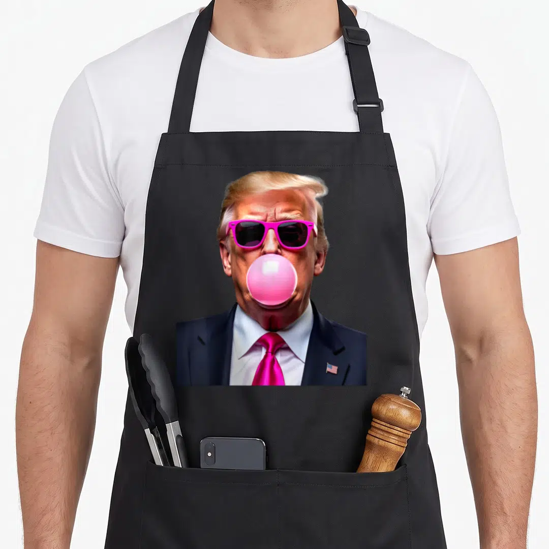 Trump funny bubble apron - Portrait of man in pink sunglasses blowing pink bubblegum wearing navy suit with flag pin — shown on a black cotton canvas apron against a white background