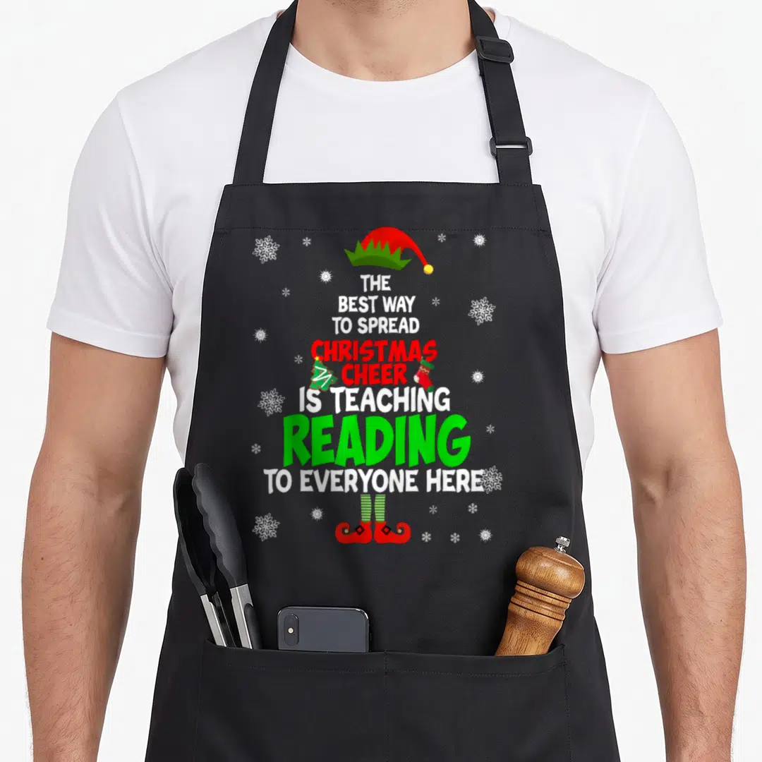 Cheer christmas apron - Stacked text spread Christmas cheer teaching reading with elf hat shoes and snowflakes — shown on a black cotton canvas apron against a white background