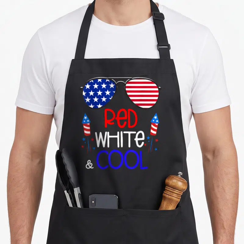Funny sunglass 4th of july apron - Aviator sunglasses with US flag lenses and red white blue text flanked by rockets — shown on a black cotton canvas apron against a white background