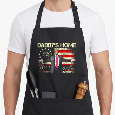 Daddy american flag apron - Donald Trump portrait with Daddy's Home 1776 We the People text on distressed flag — shown on a black cotton canvas apron against a white background
