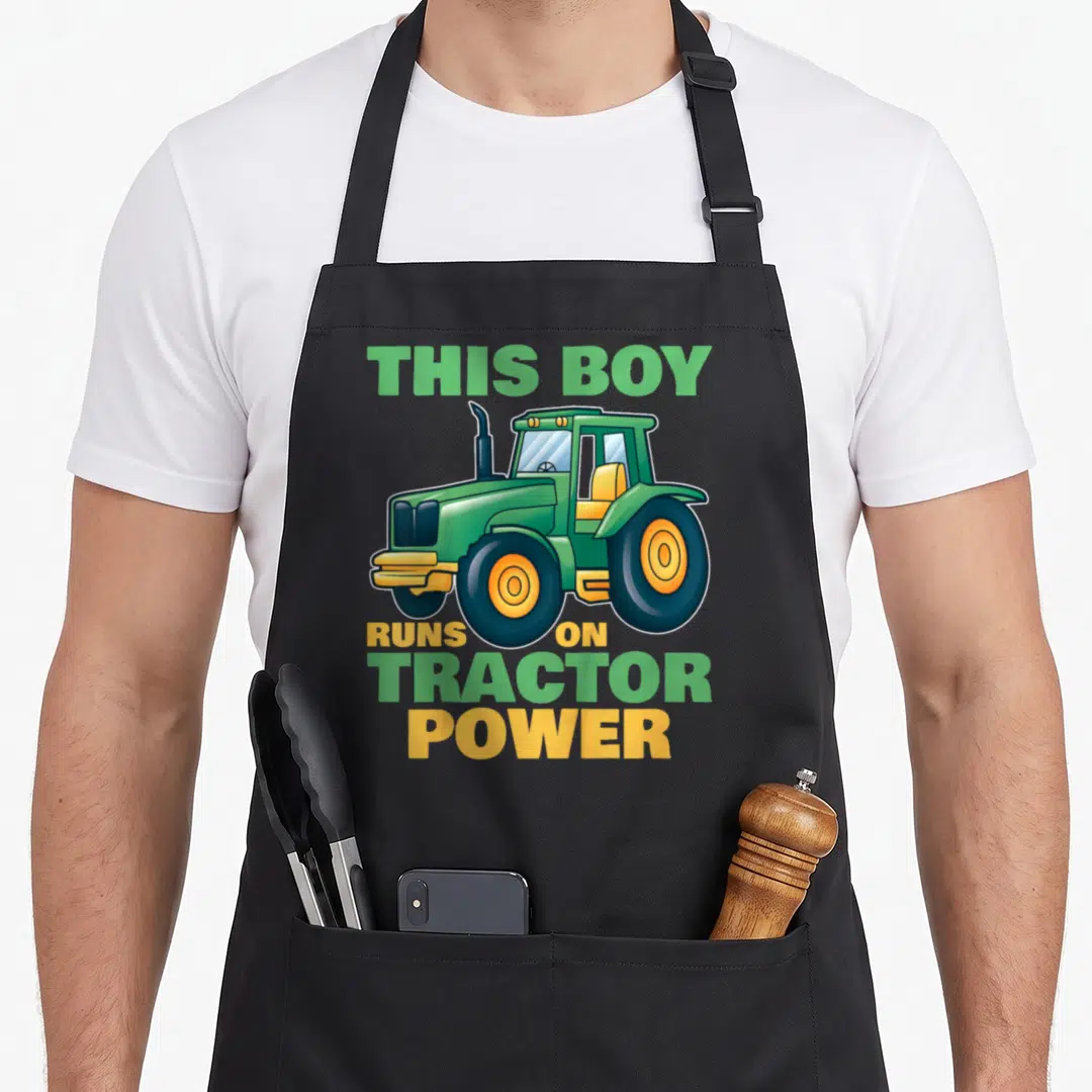 Toddler tractor girl apron - Green cartoon tractor with text This Boy Runs on Tractor Power in yellow and blue — shown on a black cotton canvas apron against a white background