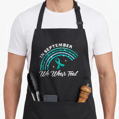 Pco rainbow apron - Teal and blue glitter rainbow arcs with awareness ribbon and text IN SEPTEMBER We Wear Teal — shown on a black cotton canvas apron against a white background
