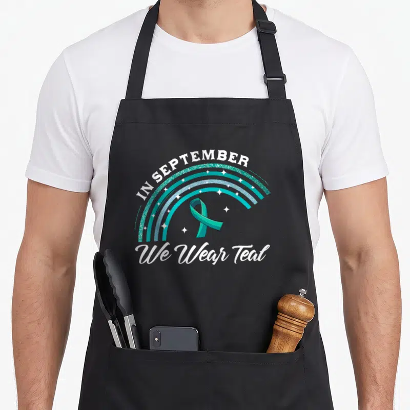 Pco rainbow apron - Teal and blue glitter rainbow arcs with awareness ribbon and text IN SEPTEMBER We Wear Teal — shown on a black cotton canvas apron against a white background