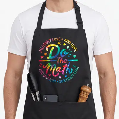 Math tie dye apron - Tie-dye text Do The Math surrounded by hearts and plus signs in rainbow colors — shown on a black cotton canvas apron against a white background