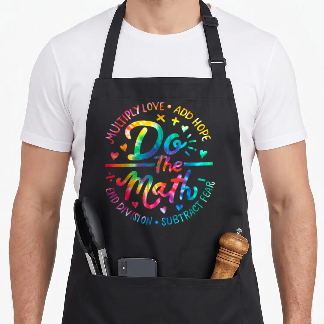Math tie dye apron - Tie-dye text Do The Math surrounded by hearts and plus signs in rainbow colors — shown on a black cotton canvas apron against a white background