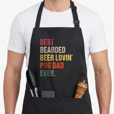 Bearded beer apron - Stacked text BEST BEARDED BEER LOVIN PUG DAD EVER in red beige yellow orange green — shown on a black cotton canvas apron against a white background