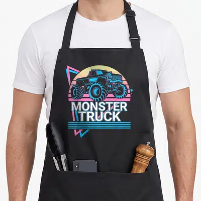 Vintage monster truck apron - Blue monster truck illustration with white text and pink triangle on yellow sun background — shown on a black cotton canvas apron against a white background