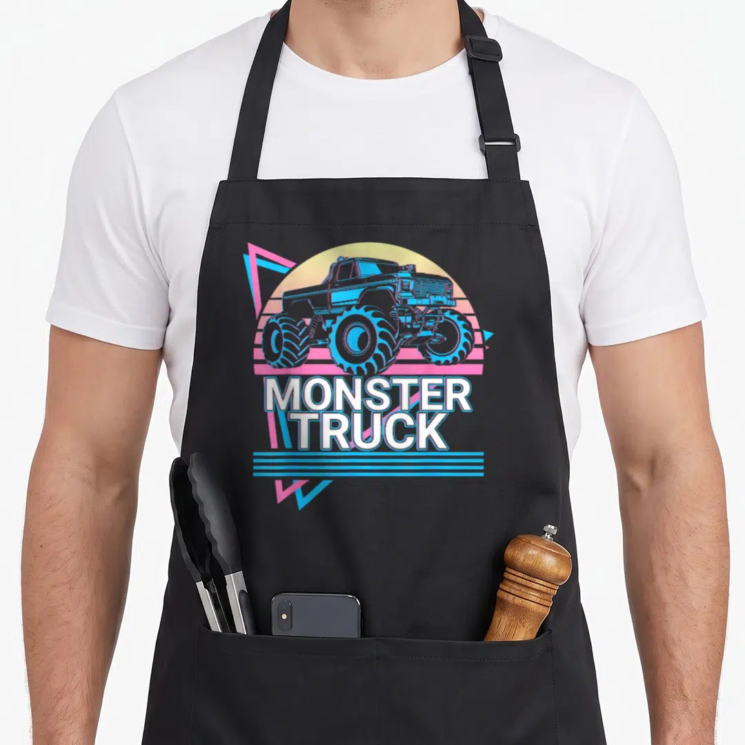 Vintage monster truck apron - Blue monster truck illustration with white text and pink triangle on yellow sun background — shown on a black cotton canvas apron against a white background