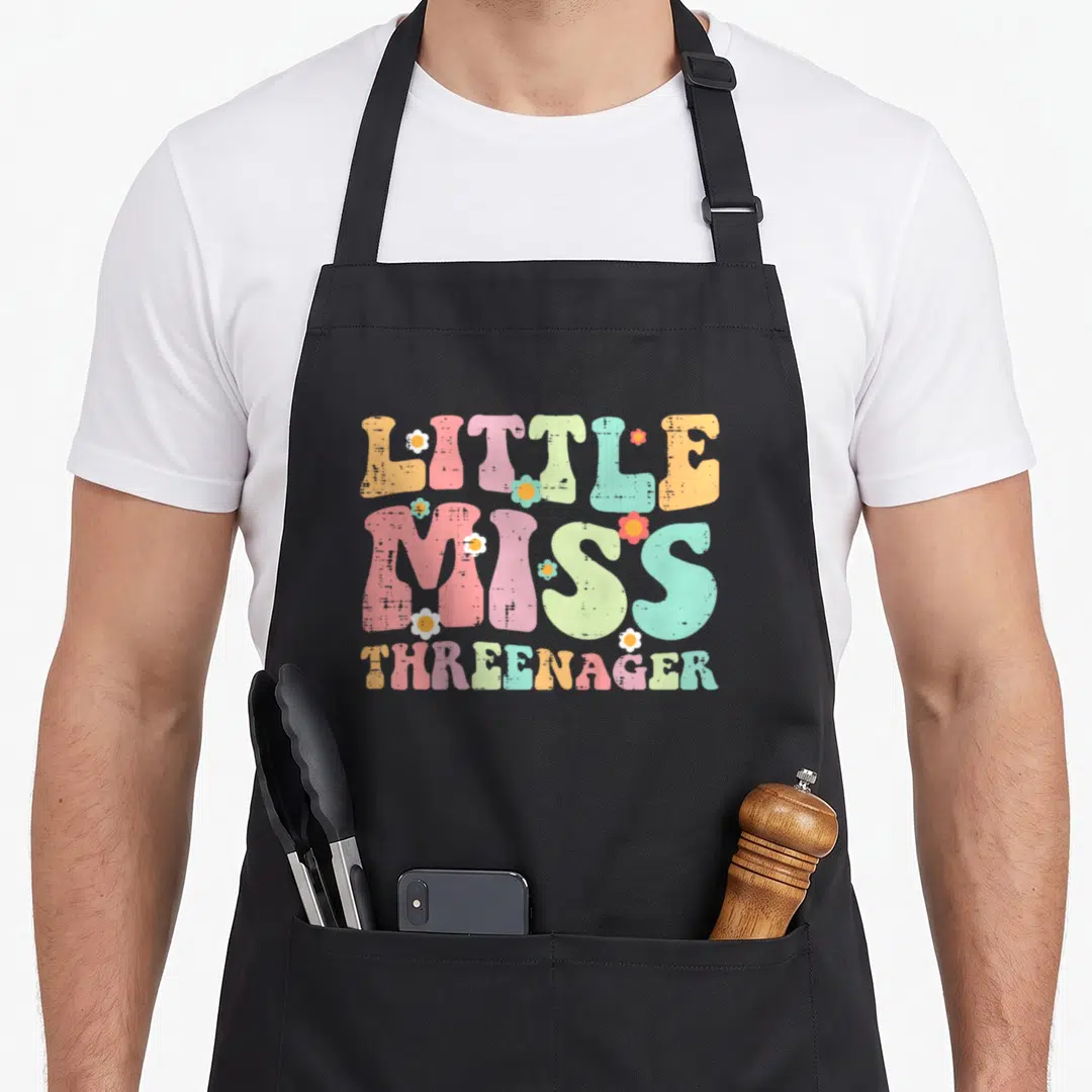 Threenager birthday apron - Retro LITTLE MISS THREENAGER text with pink blue yellow green orange flowers — shown on a black cotton canvas apron against a white background