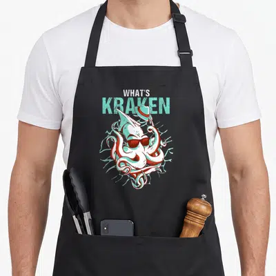 Ocean kraken apron - Cartoon kraken with sunglasses and hat under stacked text reading WHAT'S KRAKEN in teal and white — shown on a black cotton canvas apron against a white background