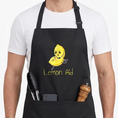 Lemonaid lemon apron - Cartoon yellow lemon doing CPR on another lemon with Lemon Aid text below — shown on a black cotton canvas apron against a white background