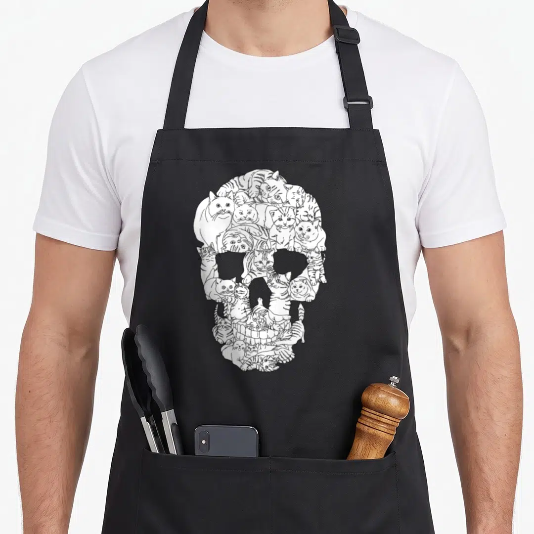 Skull kitty cat apron - White line-art skull formed by cluster of overlapping cats on black background — shown on a black cotton canvas apron against a white background
