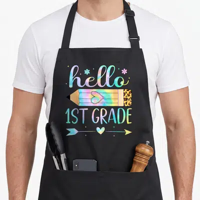 1st tie-dye apron - Hello 1st Grade tie dye text with leopard pencil and arrow — shown on a black cotton canvas apron against a white background