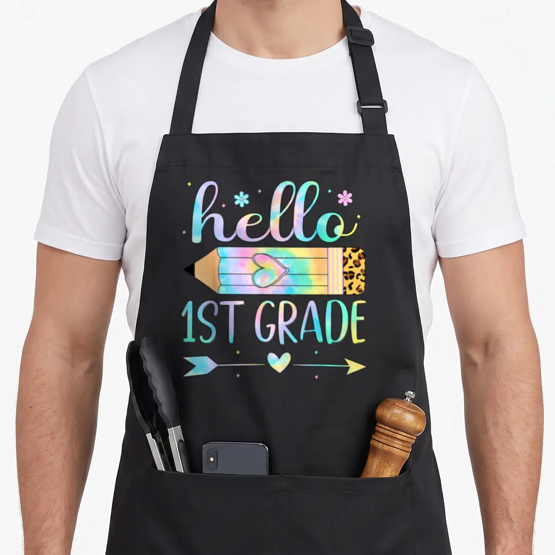 1st tie-dye apron - Hello 1st Grade tie dye text with leopard pencil and arrow — shown on a black cotton canvas apron against a white background