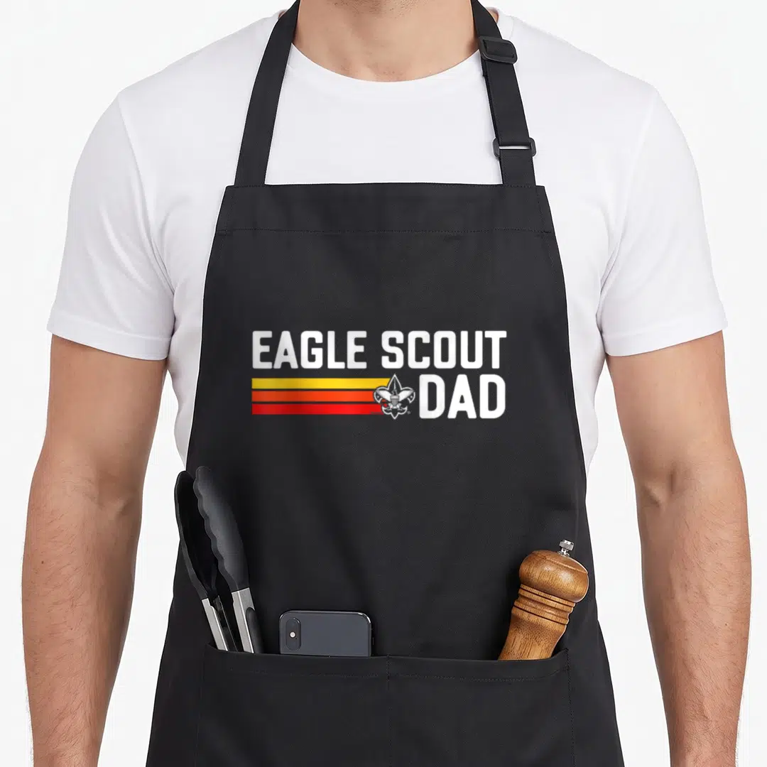 80s eagles apron - Eagle Scout Dad text with retro stripes and fleur-de-lis emblem — shown on a black cotton canvas apron against a white background