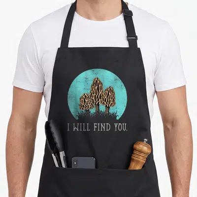 Morel mushroom apron - Three brown morels in turquoise circle with white text I WILL FIND YOU below — shown on a black cotton canvas apron against a white background