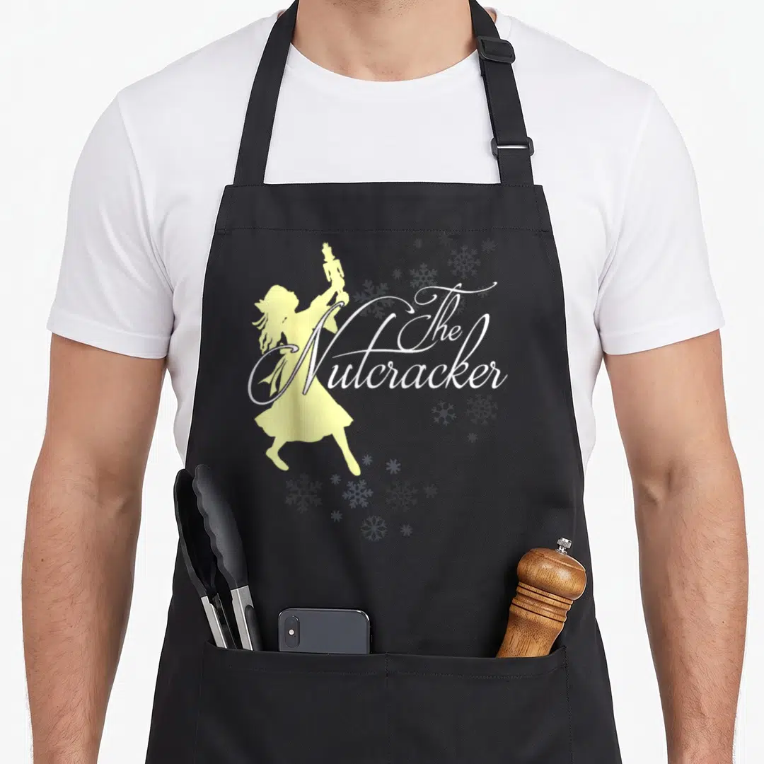 Ballerina nutcracker apron - Pale yellow ballerina silhouette holding doll with white The Nutcracker script — shown on a black cotton canvas apron against a white background