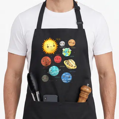 Planet astronomy life apron - Cartoon solar system with labeled Sun, Mercury, Venus, Earth, Mars, Jupiter, Saturn — shown on a black cotton canvas apron against a white background