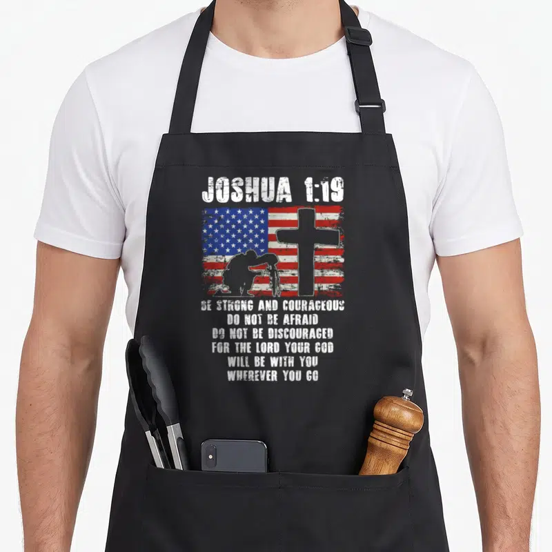 Patriotic bible verse apron - Joshua 1:19 text over distressed US flag, cross, and kneeling soldier silhouette in red — shown on a black cotton canvas apron against a white background