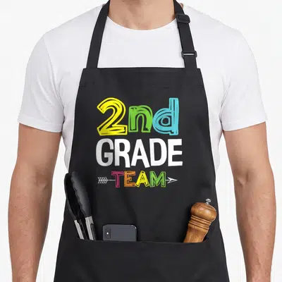 Grade squad 2nd apron - Stacked 2nd GRADE TEAM text with arrow in yellow green blue pink orange white — shown on a black cotton canvas apron against a white background