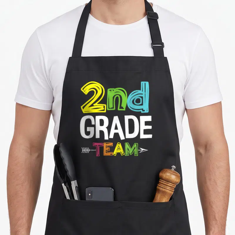 Grade squad 2nd apron - Stacked 2nd GRADE TEAM text with arrow in yellow green blue pink orange white — shown on a black cotton canvas apron against a white background