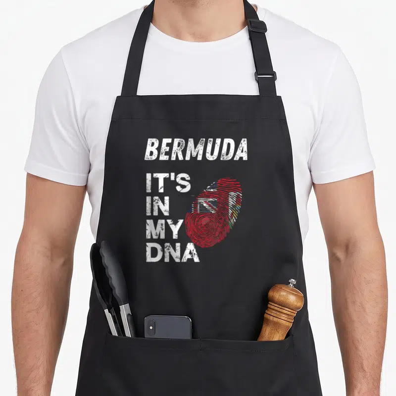 Bermuda pride apron - Stacked white text BERMUDA IT'S IN MY DNA next to a red fingerprint containing a flag — shown on a black cotton canvas apron against a white background